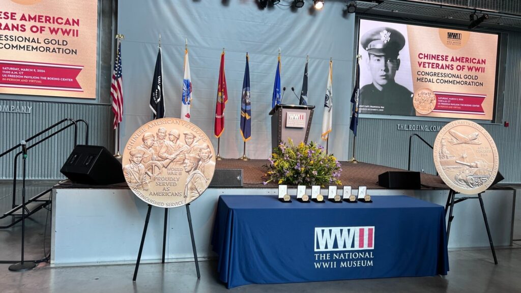 Display of large Congressional Gold Medals in front of flags and next to table with 6 Congressional Gold Medals to be presented to 6 living Chinese American WWII veterans