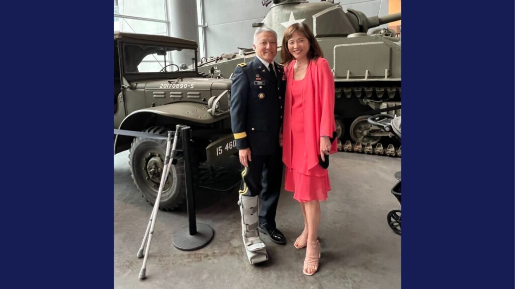 Major General Ted Wong and his wife Jeanie posing in front of a truck and tank at the National WII Museum in New Orleans