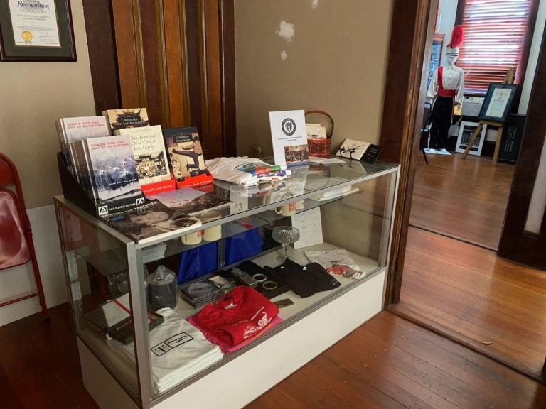 Photos of the CHSSC Bookstore showing the display case with items for sale including t-shirts, mugs, DVDs and books