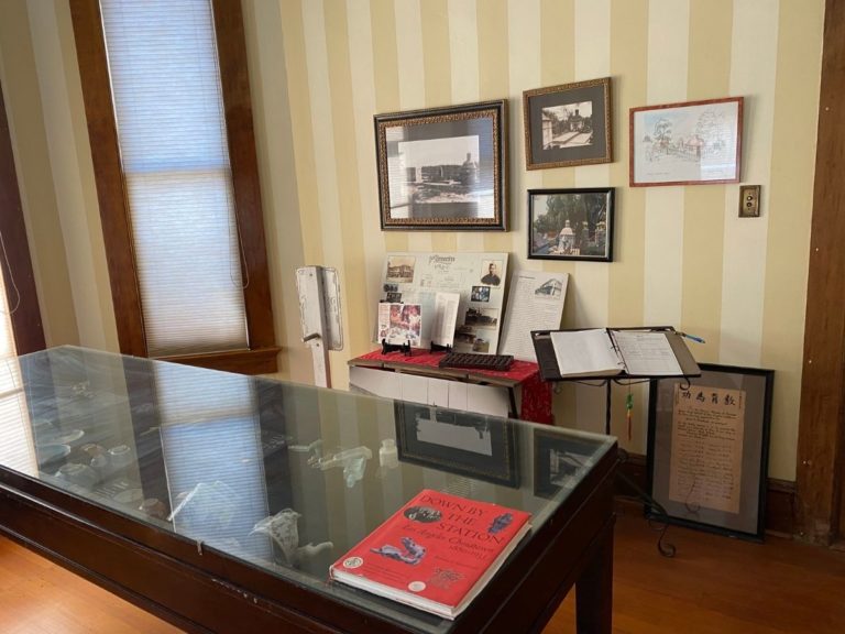 Photo of front display room with artifact display case, pictures on the wall, information sheets and sign in book