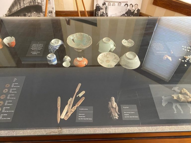 Photo of front display room showing detailed view of the artifacts in the display case with dishes, toothbrushes, and figurine