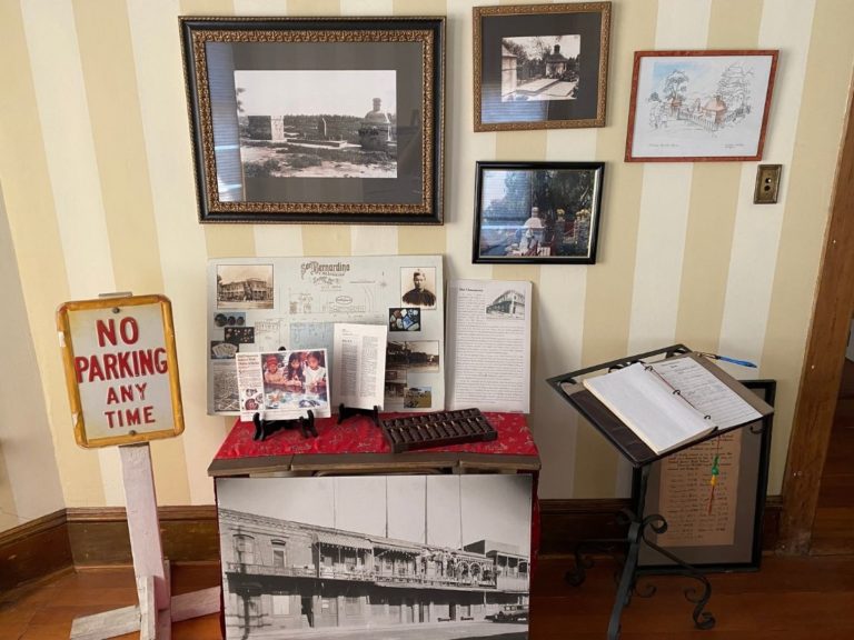 Photo of front display room showing the wall to the right of the bay windows, including pictures of the Chinese Shrine on the wall, information displays, an abacus and the sign in book