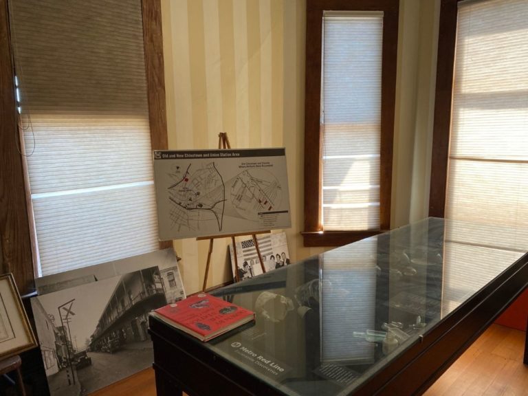 Photo of front display room facing to the left of the bay windows with artifact display case and map on an easel