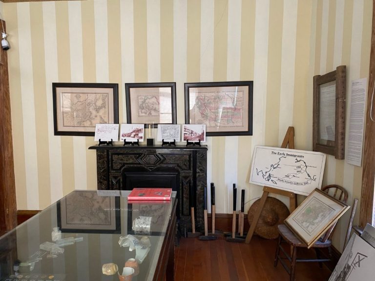Photo of front display room facing opposite of the bay windows with additional framed maps on the wall, displays and tools