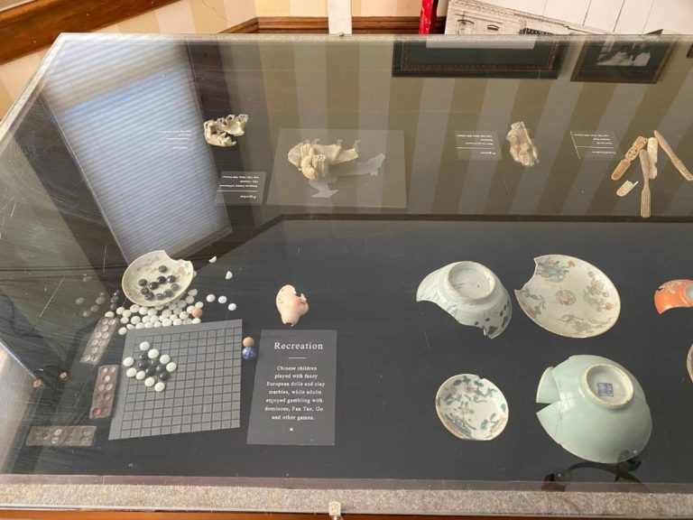 Photo of front display room showing detailed view of the artifacts in the display case including a Chinese game and dishes