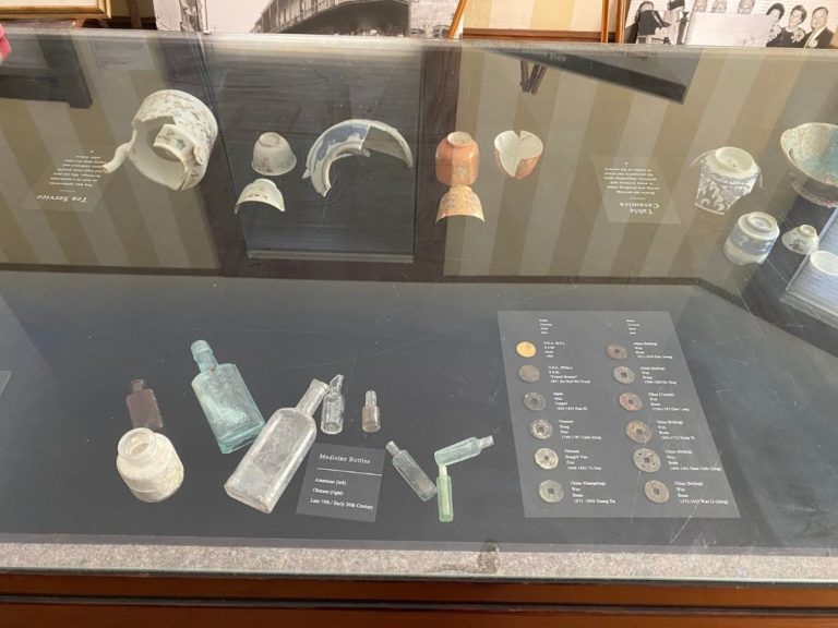 Photo of front display room showing detailed view of the artifacts in the display case with medicine bottle and Chinese coins