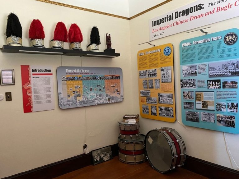 Photo of the Drum & Bugle Display room with an information posters on the front and left walls, hats on the front wall, and drums on the floor