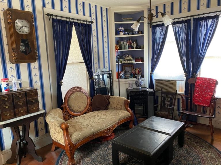 Photo of the CHSSC library showing a clock, small wooden box with 9 drawers, couch, display case in the corner, coffee table, small table with Chinese vase on top, a small and a regular size chair