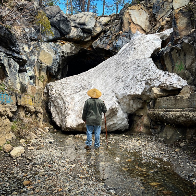 Depiction of a Chinese railroad worker standing in water in front of a railroad tunnel blocked by a huge stone