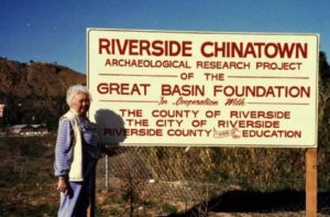 Woman standing next to a sign for the Riverside Chinatown Archaeological Research Project in 1987
